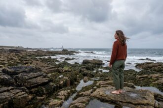 Femme contemplant le littoral breton depuis des rochers de granite à marée basse, paysage côtier sauvage en Bretagne