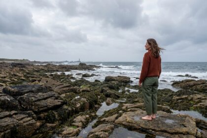Femme contemplant le littoral breton depuis des rochers de granite à marée basse, paysage côtier sauvage en Bretagne