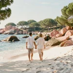 Couple romantique se promenant pieds nus sur la plage de Palombaggia en Corse, avec les rochers de granit rose et les eaux turquoise en arrière-plan