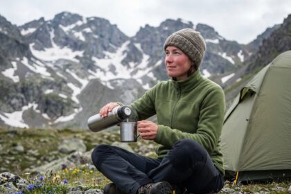 Femme en camping en montagne avec thermos et tente